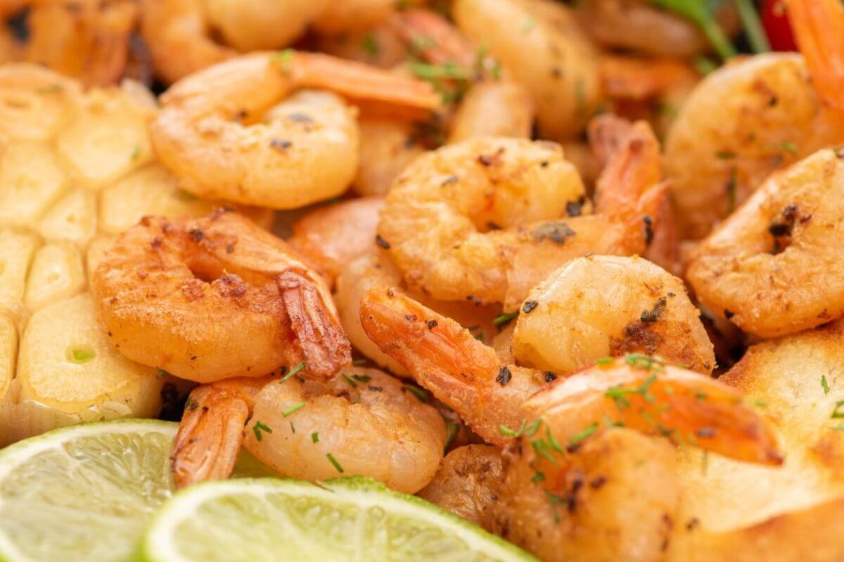 Close-up image of a plate of grilled shrimp garnished with chopped herbs. The shrimp are accompanied by toasted bread slices, grilled garlic, lime slices, and colorful vegetables like cherry tomatoes and bell peppers. This appetizing and well-seasoned dish offers a sulit experience reminiscent of top seafood restaurants in Metro Manila.