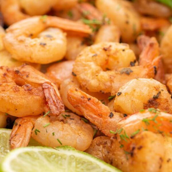 Close-up image of a plate of grilled shrimp garnished with chopped herbs. The shrimp are accompanied by toasted bread slices, grilled garlic, lime slices, and colorful vegetables like cherry tomatoes and bell peppers. This appetizing and well-seasoned dish offers a sulit experience reminiscent of top seafood restaurants in Metro Manila.