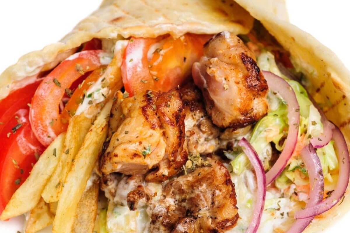 A close-up image of a gyro wrap featuring grilled pieces of seasoned meat, fresh tomato slices, red onion, lettuce, and a generous amount of fries. The ingredients are wrapped in a soft pita bread and drizzled with a creamy white sauce. This dish is one of the best places to enjoy shawarma in Metro Manila.