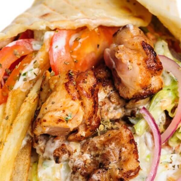 A close-up image of a gyro wrap featuring grilled pieces of seasoned meat, fresh tomato slices, red onion, lettuce, and a generous amount of fries. The ingredients are wrapped in a soft pita bread and drizzled with a creamy white sauce. This dish is one of the best places to enjoy shawarma in Metro Manila.