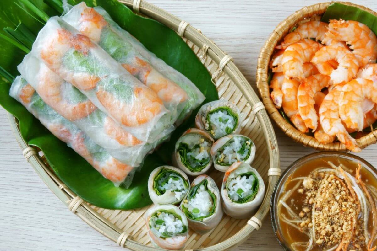 A woven tray holding fresh spring rolls filled with shrimp and vegetables rests atop a green banana leaf. Next to it, a small wicker bowl contains cooked shrimp, and another bowl is filled with brown peanut sauce garnished with crushed peanuts and sliced vegetables—a nod to authentic dining in Metro Manila's Vietnamese restaurants.