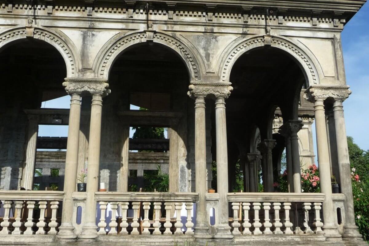 The Ruins, in silay, bacolod. The arches form a covered walkway or verandah. This sight is a must-see for any Bacolod travel guide. The structure is partially in ruins with visible greenery in the background and potted plants along the balustrade.