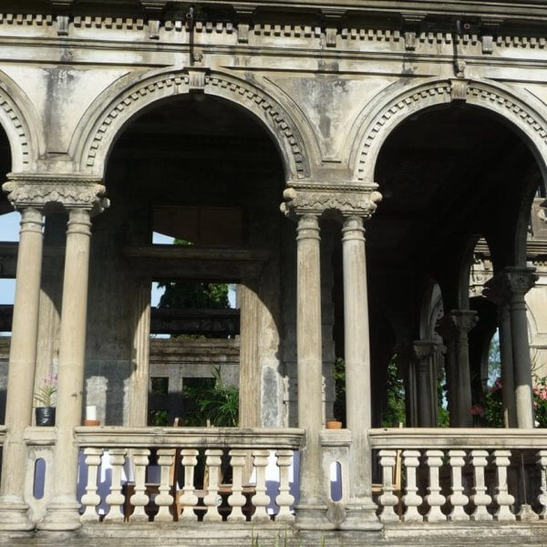 The Ruins, in silay, bacolod. The arches form a covered walkway or verandah. This sight is a must-see for any Bacolod travel guide. The structure is partially in ruins with visible greenery in the background and potted plants along the balustrade.