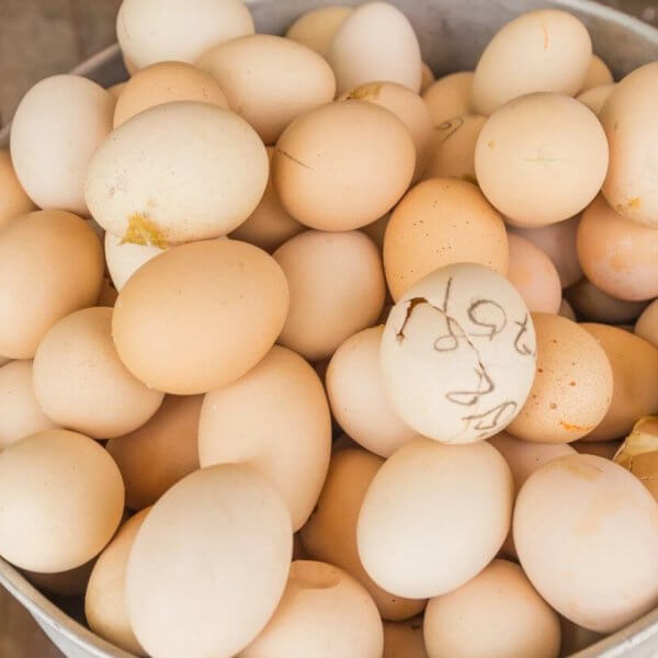 A large metal bucket filled with Balut, some bearing small dirt stains or marks on their shells. The bucket, featuring two handles on either side, rests on a rustic surface, evoking the setting of a farm or market – ideal for Balut suppliers in Metro Manila.