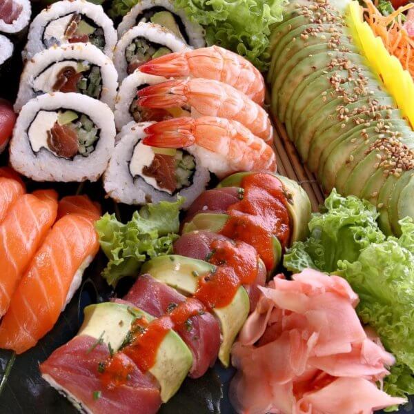 A colorful sushi platter displayed artfully at Okada Manila, one of the best restaurants. The assortment includes culinary gems like nigiri sushi with salmon and tuna, various sushi rolls with fillings like vegetables and seafood topped with avocado and sauces, shrimp, garnished with ginger, wasabi and lettuce.