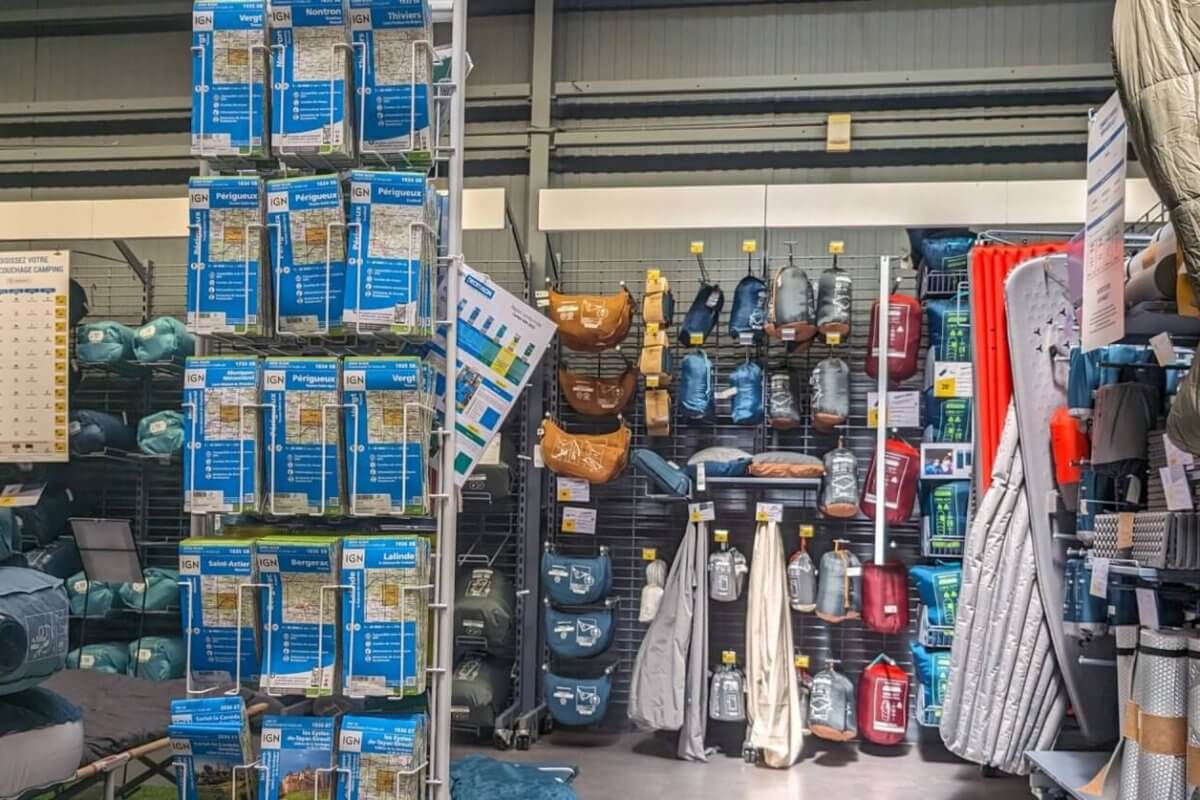 A well-organized camping gear section in one of the best camping stores in Metro Manila displays an array of neatly arranged outdoor equipment. On the left, air mattresses and travel pillows are stacked on shelves. The center showcases various hydration packs and bags. The right features sleeping bags and camping mats hanging on hooks.