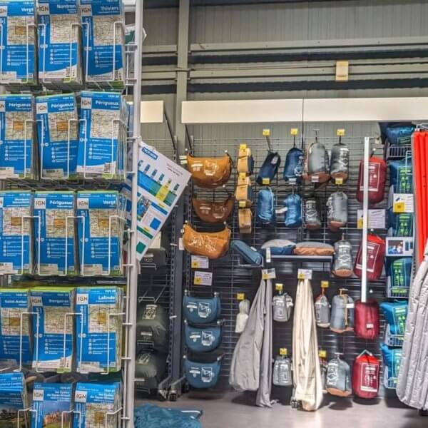 A well-organized camping gear section in one of the best camping stores in Metro Manila displays an array of neatly arranged outdoor equipment. On the left, air mattresses and travel pillows are stacked on shelves. The center showcases various hydration packs and bags. The right features sleeping bags and camping mats hanging on hooks.