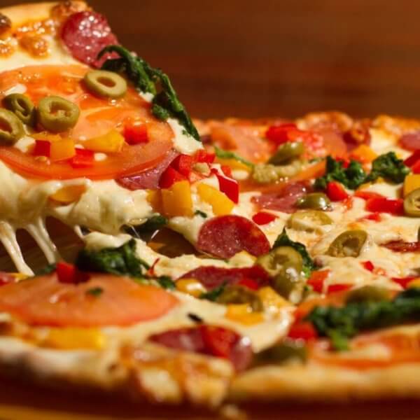 pizza at one of the best restaurants in Festival Mall. The pizza is topped with melted cheese, pepperoni, tomato slices, green olives, red bell peppers, and leafy greens. The crust is golden brown, and the cheese is stretchy as the slice is pulled away.