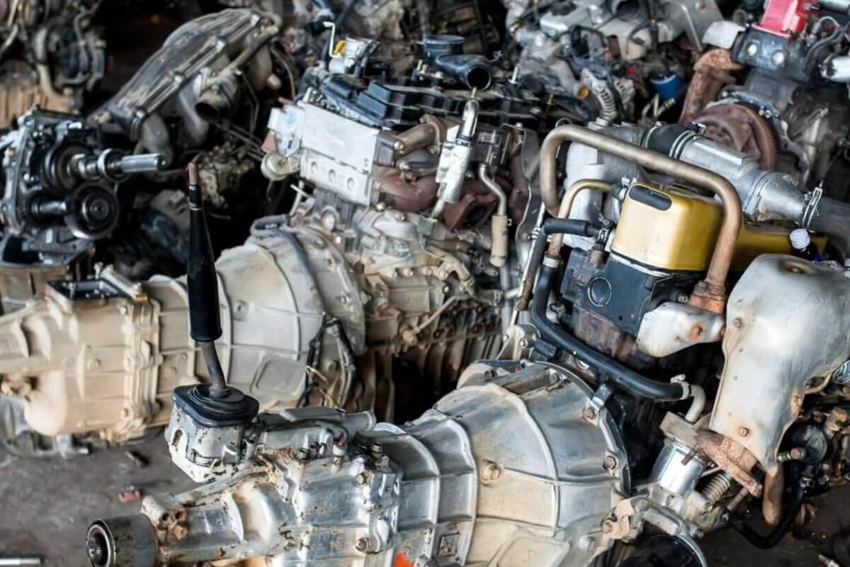 A cluttered workshop in Metro Manila with multiple disassembled car engines and gearboxes. The engines are placed close together on the floor, showing components like turbochargers, exhaust manifolds, and fuel injection systems. Some tools and small parts from the 35 Best Junk Shops are scattered around the area.