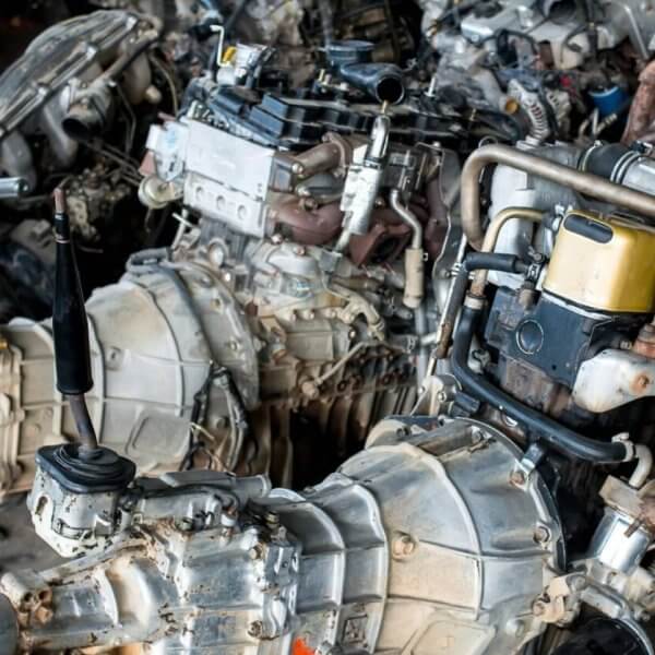 A cluttered workshop in Metro Manila with multiple disassembled car engines and gearboxes. The engines are placed close together on the floor, showing components like turbochargers, exhaust manifolds, and fuel injection systems. Some tools and small parts from the 35 Best Junk Shops are scattered around the area.