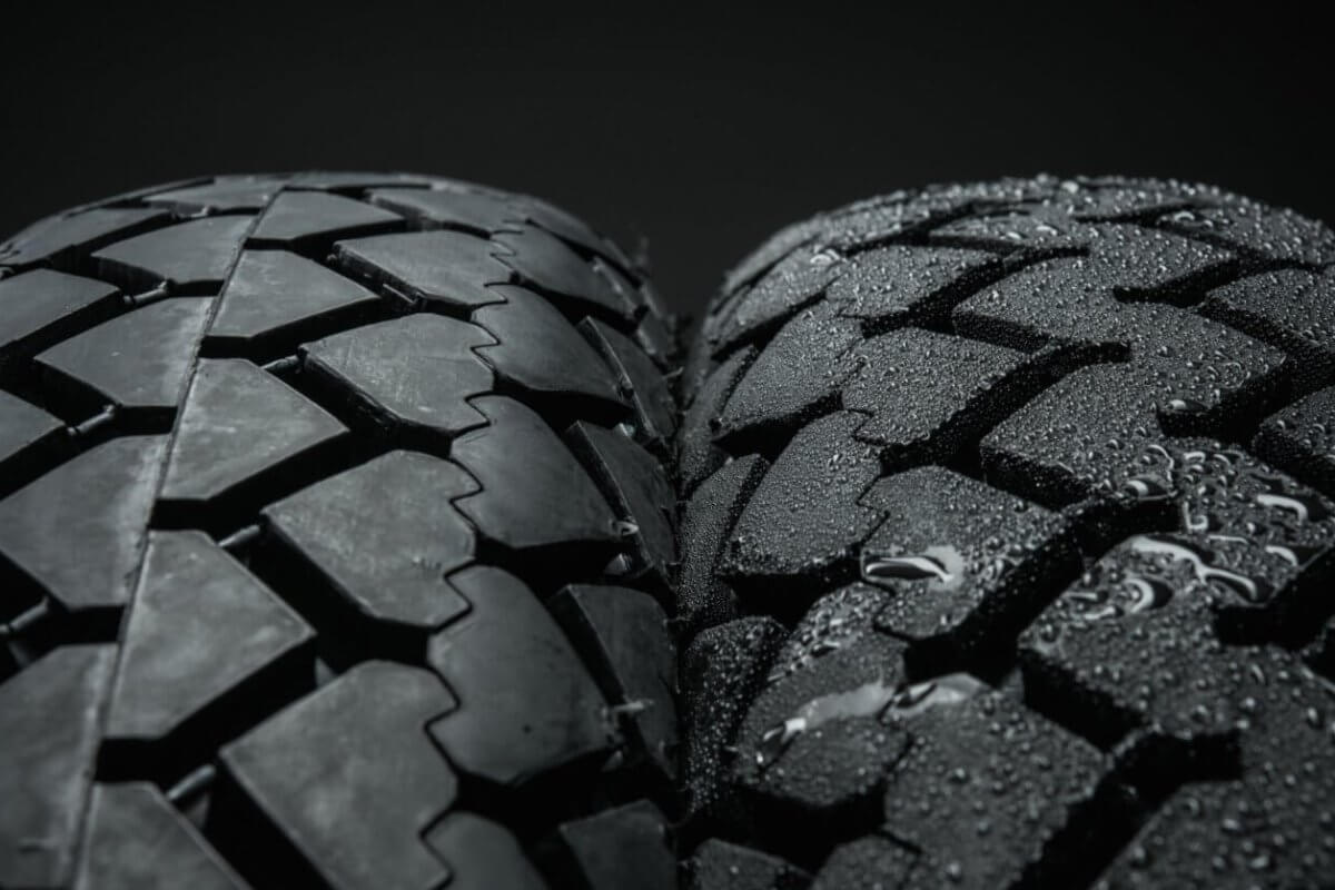 Close-up view of two motorcycle tires side by side against a black background. The tire on the left features a smooth tread, while the tire on the right has a rough tread pattern and is covered in water droplets, suggesting wet conditions. Both treads have interlocking block designs from top suppliers in Metro Manila.