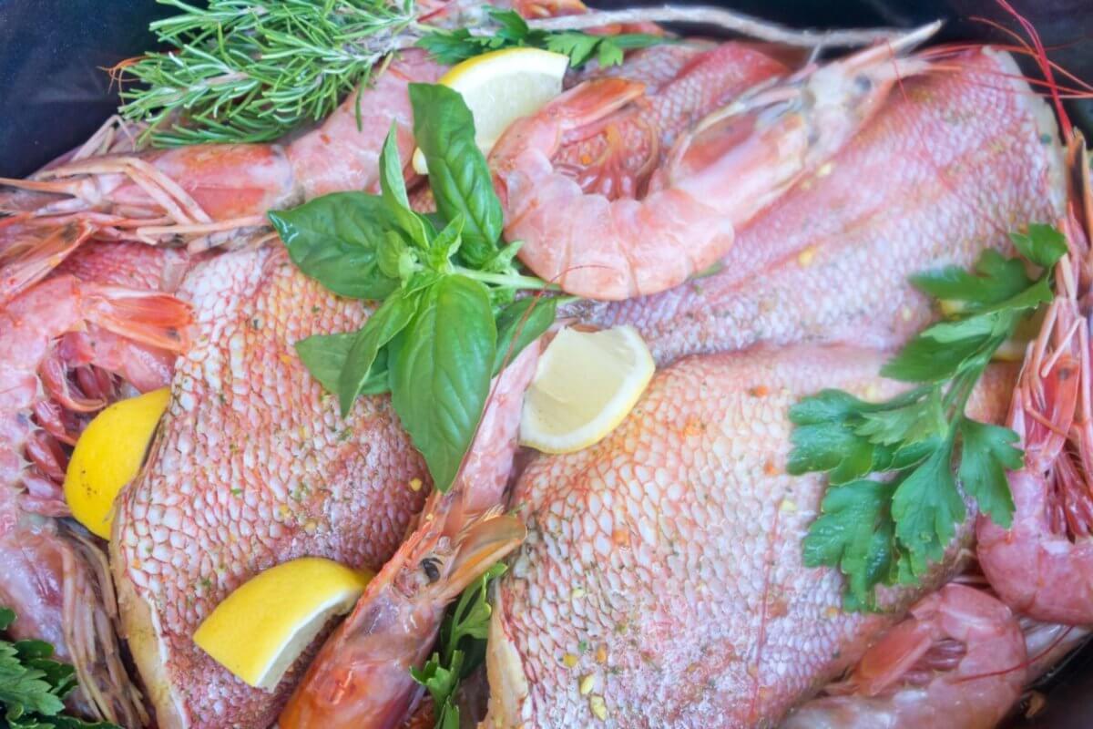 A seafood dish featuring whole fish and shrimp garnished with fresh herbs, including parsley and rosemary, is displayed. Lemon wedges are scattered throughout the arrangement, adding a vibrant contrast to the pink and red hues of the seafood, reminiscent of a Panglao feast.