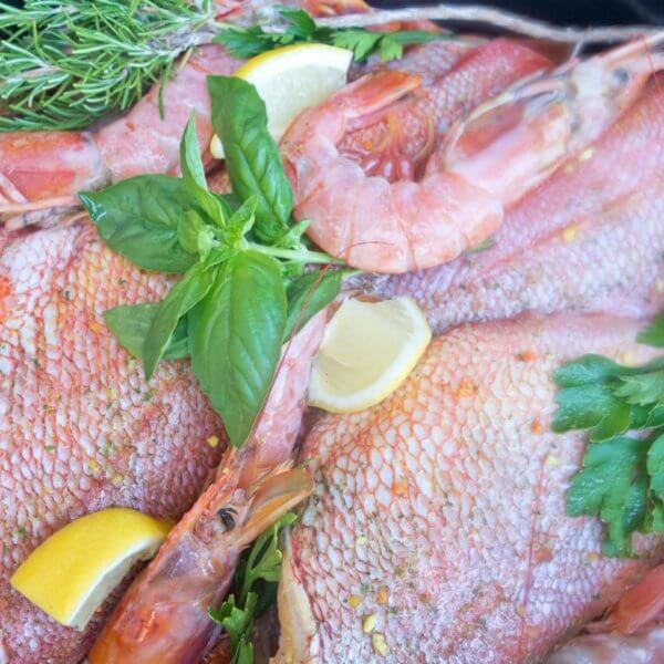 A seafood dish featuring whole fish and shrimp garnished with fresh herbs, including parsley and rosemary, is displayed. Lemon wedges are scattered throughout the arrangement, adding a vibrant contrast to the pink and red hues of the seafood, reminiscent of a Panglao feast.