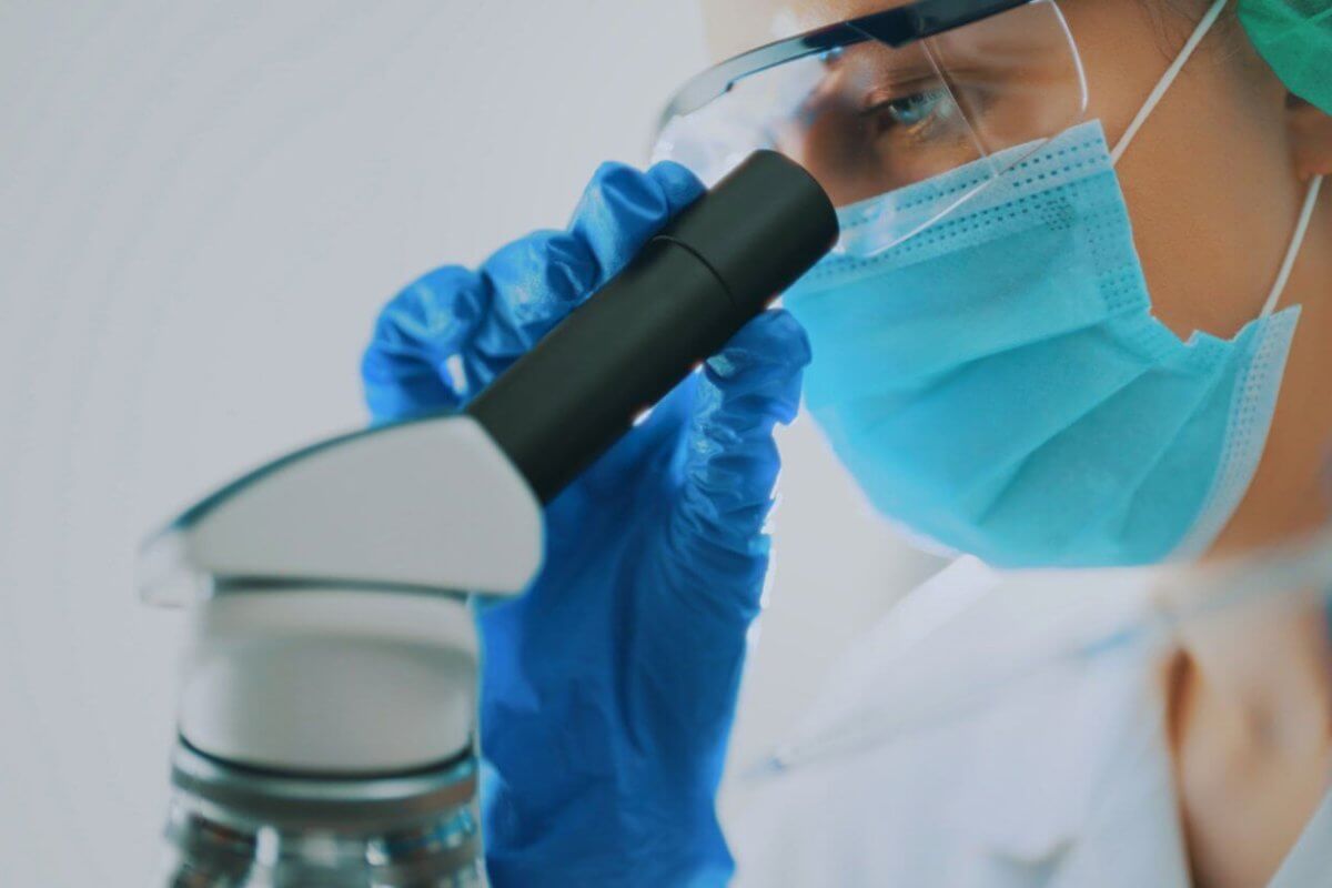 A pathologist wearing a protective face mask, goggles, and blue gloves, is closely examining a sample through a microscope. The technician's focus is evident as they work in a well-lit, sterile environment. This image highlights the meticulous scientific research and expert care one can expect from the best pathologists in Metro Manila.
