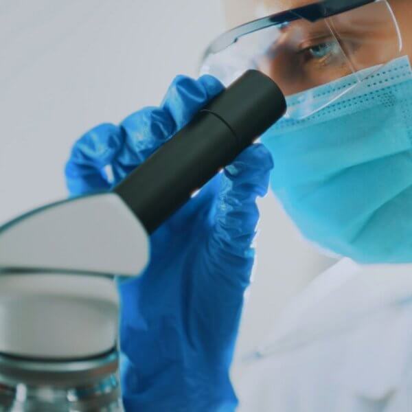 A pathologist wearing a protective face mask, goggles, and blue gloves, is closely examining a sample through a microscope. The technician's focus is evident as they work in a well-lit, sterile environment. This image highlights the meticulous scientific research and expert care one can expect from the best pathologists in Metro Manila.