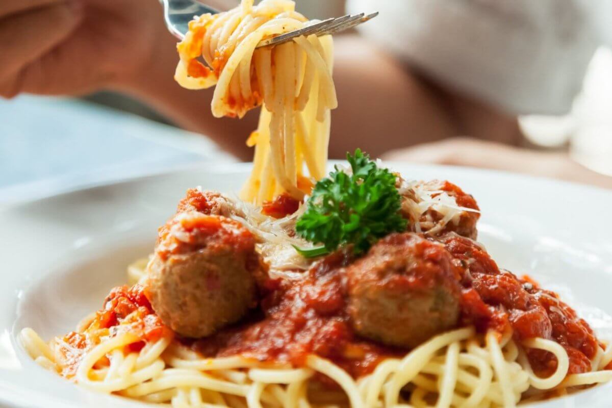 spaghetti topped with red tomato sauce, meatballs, grated cheese, and a sprig of parsley. A person is twirling the pasta around a fork, with the focus on the forkful of spaghetti being lifted from the plate at one of BGC's 46 Must-Try Restaurants near SM Aura.