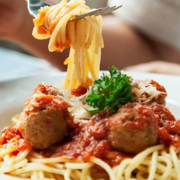 spaghetti topped with red tomato sauce, meatballs, grated cheese, and a sprig of parsley. A person is twirling the pasta around a fork, with the focus on the forkful of spaghetti being lifted from the plate at one of BGC's 46 Must-Try Restaurants near SM Aura.