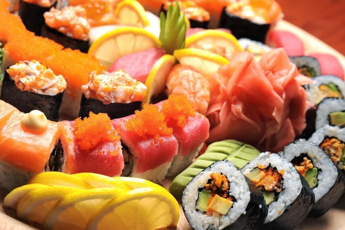 A wooden platter from sulit eats at SM Dasmariñas is filled with a variety of colorful sushi rolls and sashimi. The assortment includes rolls topped with salmon, tuna, roe, and avocado, alongside garnishes of lemon slices, pickled ginger, and wasabi. The presentation is vibrant and visually appealing.