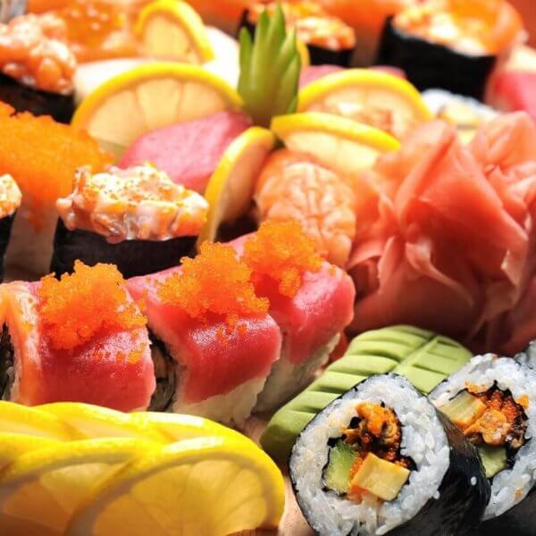 A wooden platter from sulit eats at SM Dasmariñas is filled with a variety of colorful sushi rolls and sashimi. The assortment includes rolls topped with salmon, tuna, roe, and avocado, alongside garnishes of lemon slices, pickled ginger, and wasabi. The presentation is vibrant and visually appealing.