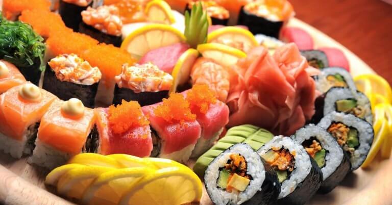 A wooden platter from sulit eats at SM Dasmariñas is filled with a variety of colorful sushi rolls and sashimi. The assortment includes rolls topped with salmon, tuna, roe, and avocado, alongside garnishes of lemon slices, pickled ginger, and wasabi. The presentation is vibrant and visually appealing.
