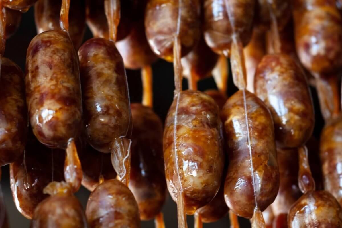 Close-up of several rows of sausages hanging vertically by beige strings. The sausages have a brownish color with visible spices embedded in the meat. The links appear glossy and slightly uneven, indicating they are likely homemade or artisanal. This delicacy could be a highlight at one of Davao's 42 Best Restaurants in SM Lanang.