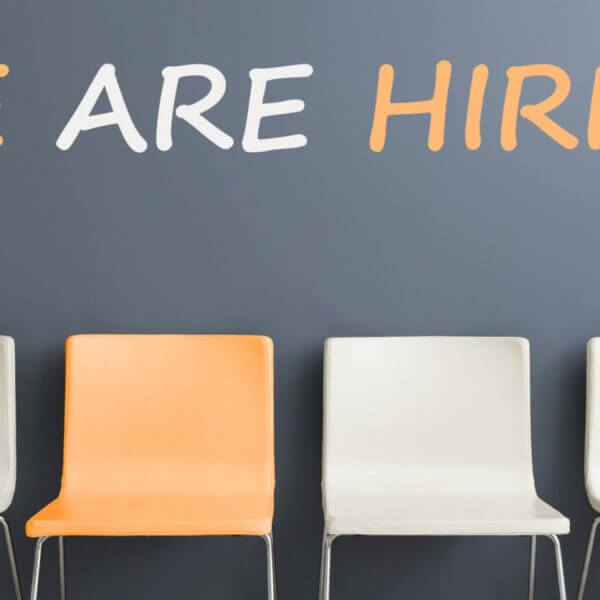 Four chairs are positioned in a row against a gray wall. The first, third, and fourth chairs are white, while the second chair is orange. Above them, the wall displays "WE ARE HIRING" in large white and orange letters—a familiar sight for those navigating job searches and employment agencies in Metro Manila.