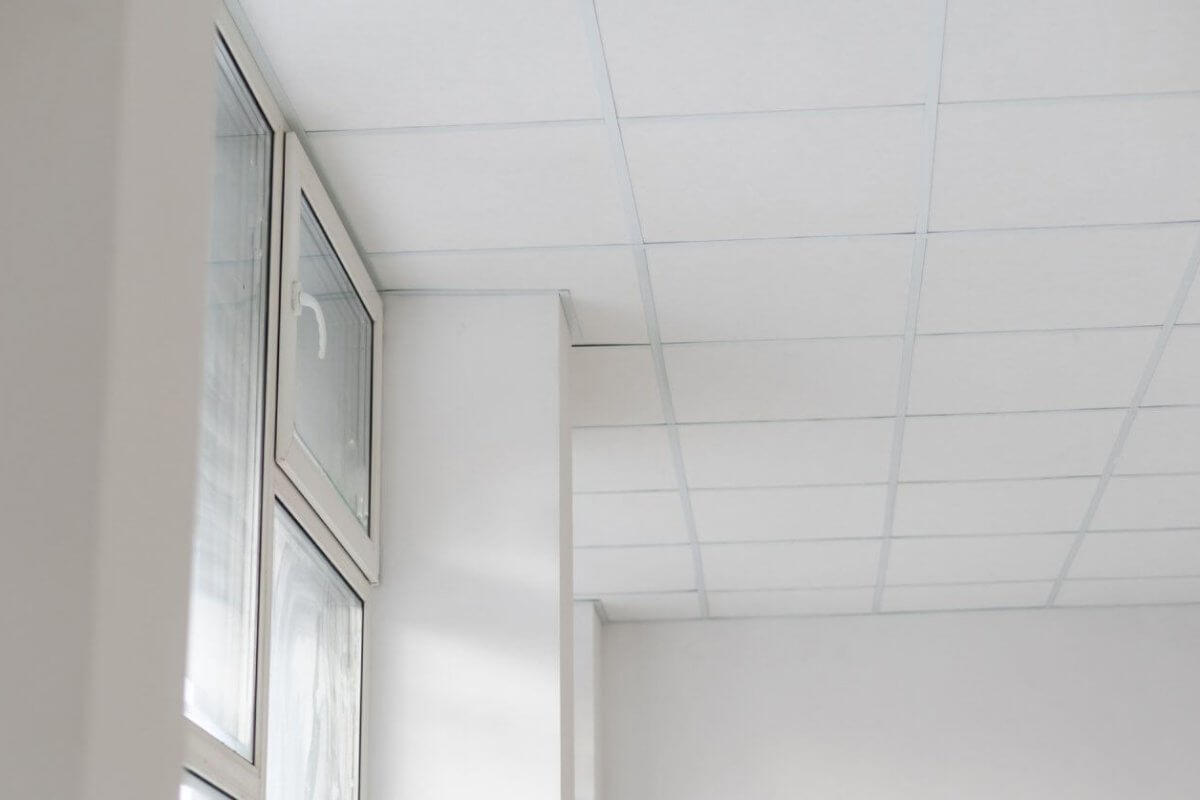 The white room features a grid-patterned drop ceiling with high-quality ceiling tiles, and large windows on the left side let in natural light.