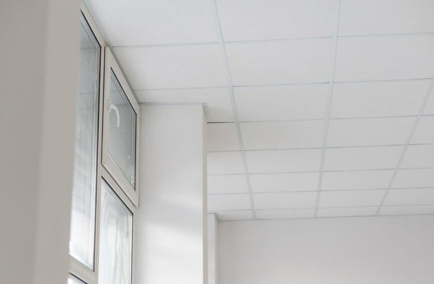 The white room features a grid-patterned drop ceiling with high-quality ceiling tiles, and large windows on the left side let in natural light.