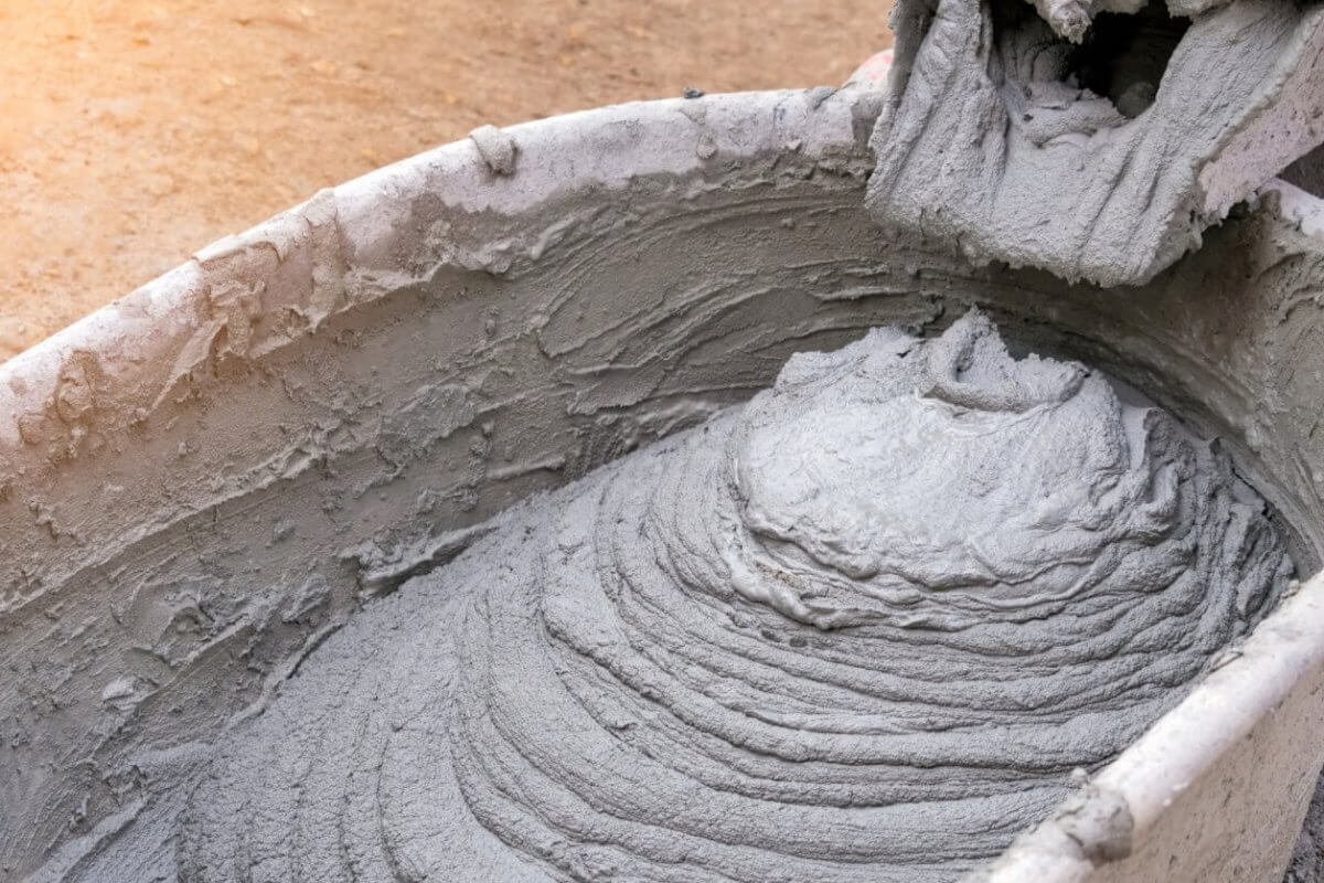 A close-up of wet cement being poured into a wheelbarrow from a mixer, forming a swirling pattern with rough texture. The wheelbarrow is slightly stained, echoing the bustling construction sites in Metro Manila, where dirt and cement suppliers ensure seamless progress amidst splatters.