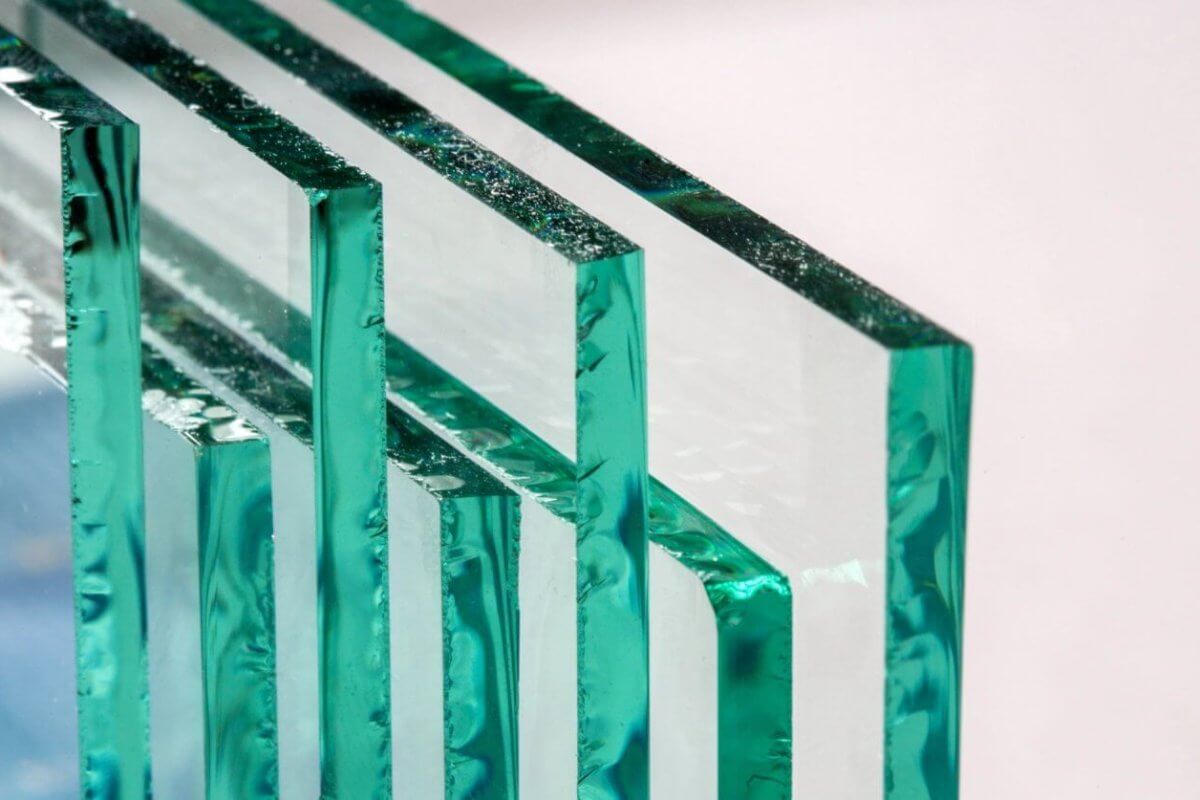 Close-up of four rectangular glass panes, supplied by leading glass suppliers in Metro Manila, standing upright and lined up horizontally against a neutral background. The edges show a green tint, with surfaces reflecting light to create a layered, transparent effect that highlights the clarity and texture.