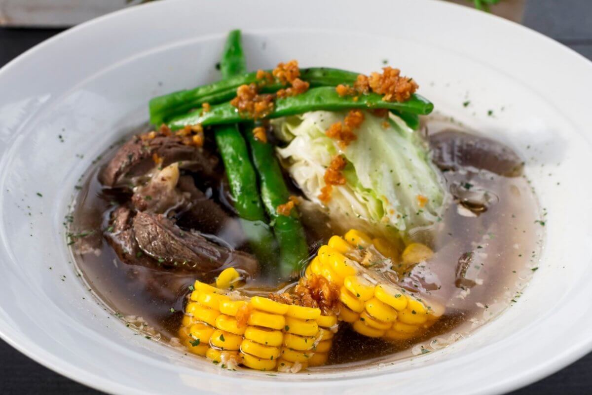 A bowl of the best soup in Batangas City, featuring tender beef, sweet corn, crisp cabbage, and fresh green beans in a clear broth, offers a delightful taste that local restaurants proudly serve.