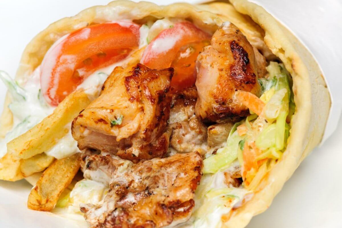 Close-up of a chicken wrap with grilled meat, lettuce, tomatoes, fries, and creamy sauce, wrapped in flatbread—one of the 23 Best dishes you'll find at top restaurants in Marawi City.
