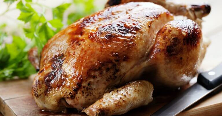 Golden roasted chicken on a wooden board with herbs, reminiscent of the savory delights you'd find at the best restaurants around. A knife is placed beside it, ready to carve into this culinary masterpiece.
