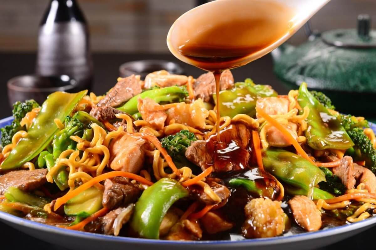 A plate of stir-fried noodles with beef, chicken, broccoli, and bell peppers being topped with soy sauce provides a mouth-watering experience. You can savor this delectable dish at one of the best restaurants in Robinsons Galleria.