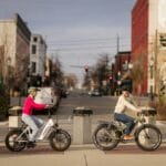 Two commuters riding electric bikes along a city street in the Philippines, the type of e-bike now restricted from major national roads under LTO's 2026 rules