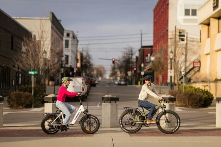Two commuters riding electric bikes along a city street in the Philippines, the type of e-bike now restricted from major national roads under LTO's 2026 rules