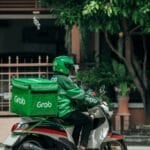 Grab delivery rider on a motorcycle with the green Grab delivery bag, representing the GrabFood and GrabCar discounts included in a GrabUnlimited subscription in the Philippines