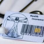 Philippine health card (HMO / health insurance card) placed next to a stethoscope, representing the choice between a basic health card and a full HMO plan in the Philippines