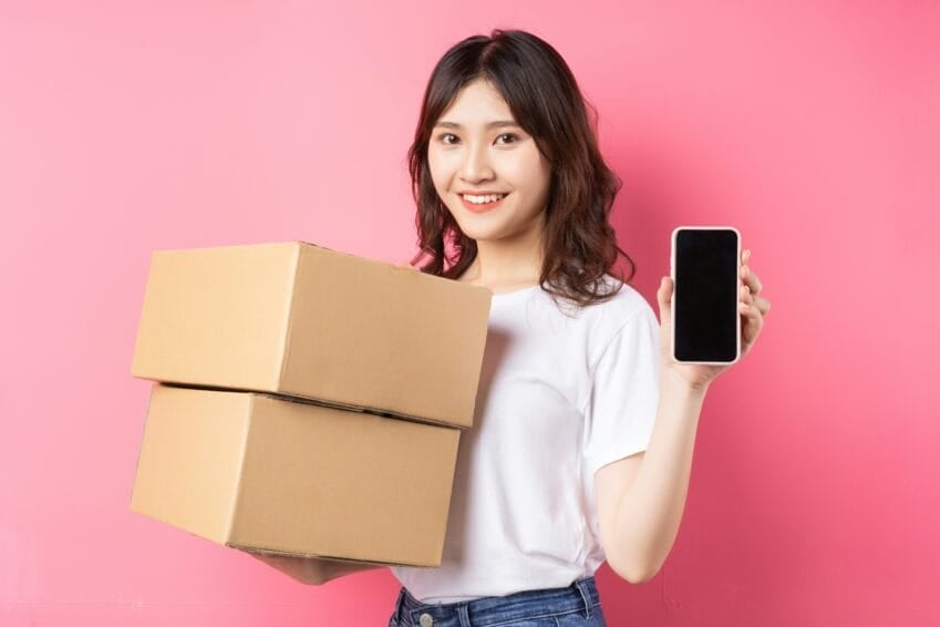 Filipino online shopper holding a delivered package box while checking a return/refund request on her phone after receiving a defective item from Shopee, Lazada, or TikTok Shop