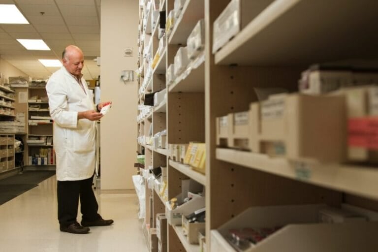 Pharmacist examining a medicine box at the pharmacy counter, checking generic drug registration in the Philippines