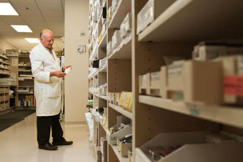 Pharmacist examining a medicine box at the pharmacy counter, checking generic drug registration in the Philippines