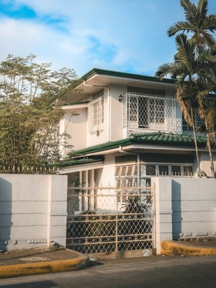 Two-story Philippine subdivision house with white facade and green tile roof, the kind of property a renting-vs-buying decision in the Philippines usually comes down to