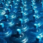 Water Refilling Station vs. Bottled Water Delivery: Which Is Actually Sulit in the Philippines? (2026 Guide) Rows of blue 5-gallon water containers, the kind refilled at Philippine water refilling stations or delivered by brands like Summit and Absolute