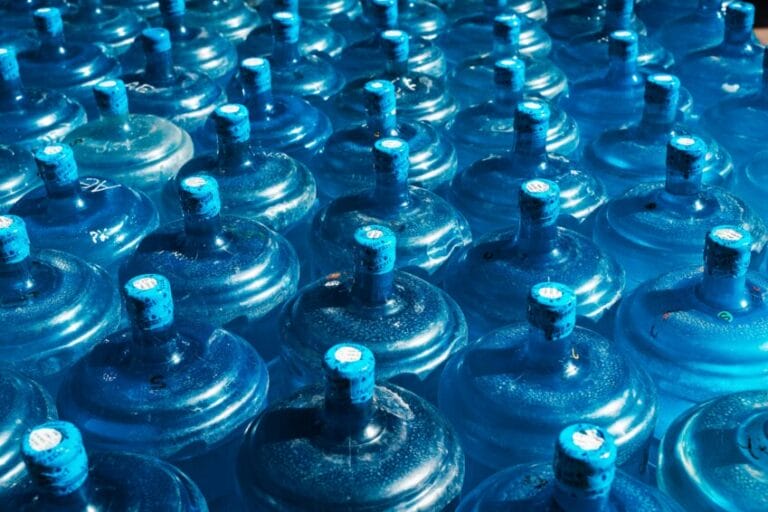 Rows of blue 5-gallon water containers, the kind refilled at Philippine water refilling stations or delivered by brands like Summit and Absolute