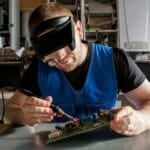 Technician repairing an appliance's electronic circuit board with a multimeter, representing a warranty repair at a TCL or budget-brand appliance service center in the Philippines