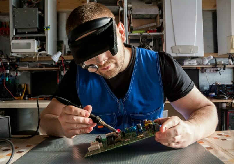 Technician repairing an appliance's electronic circuit board with a multimeter, representing a warranty repair at a TCL or budget-brand appliance service center in the Philippines