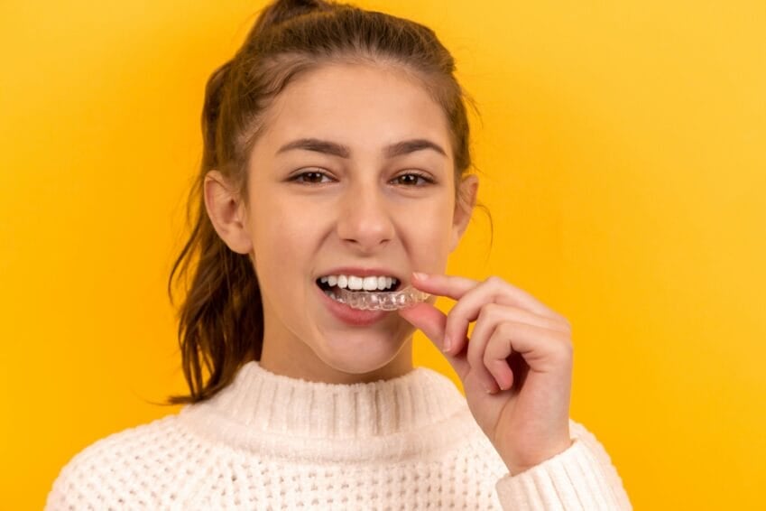 Close-up of a clear plastic dental aligner being placed over teeth, illustrating the Invisalign clear-aligner option compared to traditional braces in the Philippines