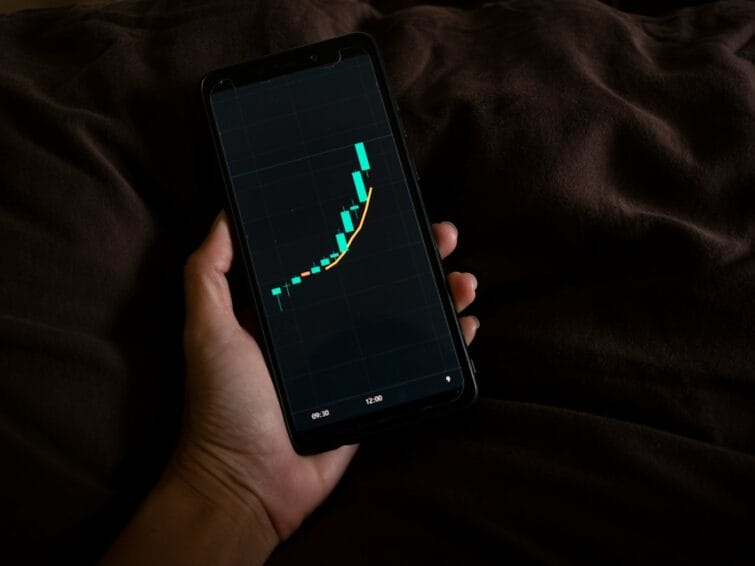 Hand holding a smartphone showing a stock/investment growth chart, representing checking a UITF, mutual fund, or GInvest balance in the Philippines