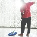 Household helper with a broom and cleaning bucket doing domestic work in a Philippine home, illustrating the kasambahay agency vs. direct hire decision