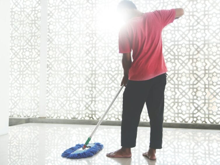 Household helper with a broom and cleaning bucket doing domestic work in a Philippine home, illustrating the kasambahay agency vs. direct hire decision